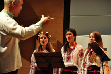 Dyrygujący mężczyzna, na drugim planie trzy kobiety