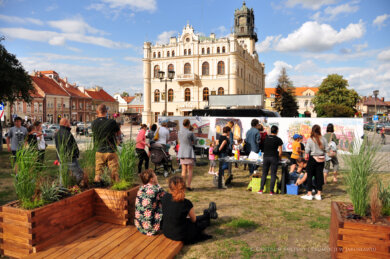 Kulturalne Lato w Mieście Z przodu - dwie osoby siedzące na podeście, z tyłu grupa ludzi malująca na ściance