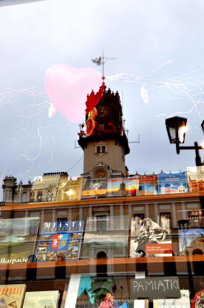 Wieża zegarowa jarosławskiego ratusza przystojona czerwonymi walentynkowymi balonami w odbiciu witryny wystawowej Centrum Informacji Turystyczno-Kulturalnej