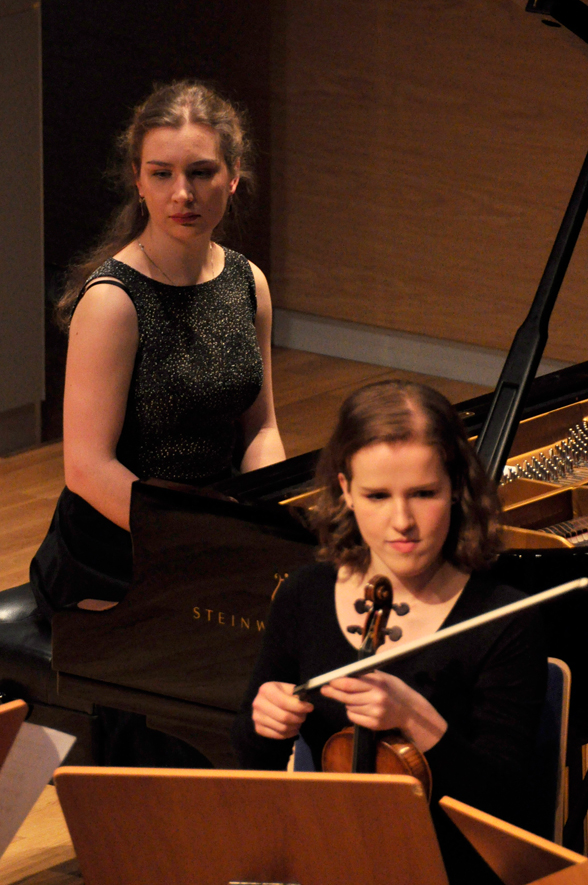 Kobieta ze skrzypcami, w tle kobieta przy fortepianie