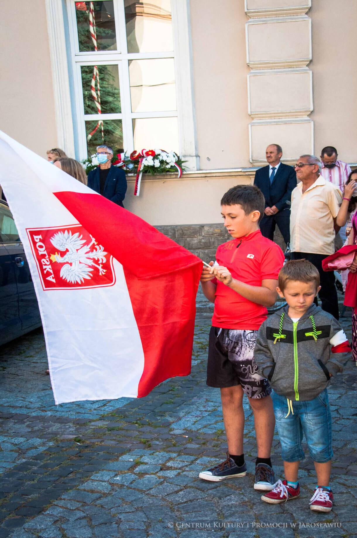 mali uczestnicy uroczystości trzymają w rękach polską flagę
