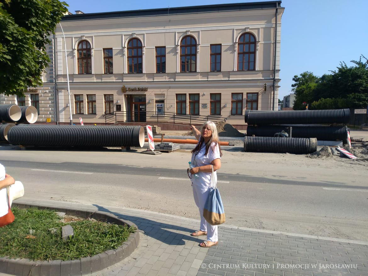 Przewodnik Joanna Płocica pokazująca budynek po drugiej stronie ulicy
