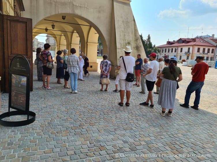 Grupa ludzi przed Kamienicą Attawantich, w tle podcienia Kamienicy Orsettich