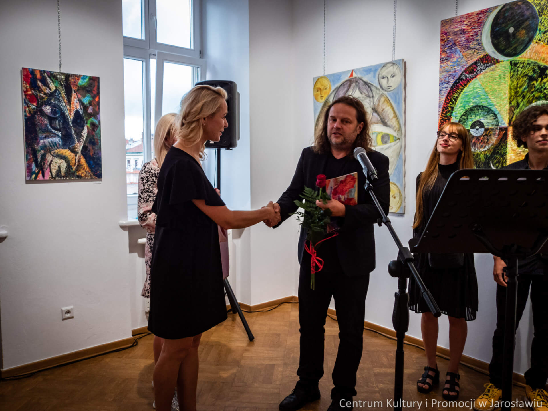 kustosz wystawy wręcza artyście pamiątkowa różę