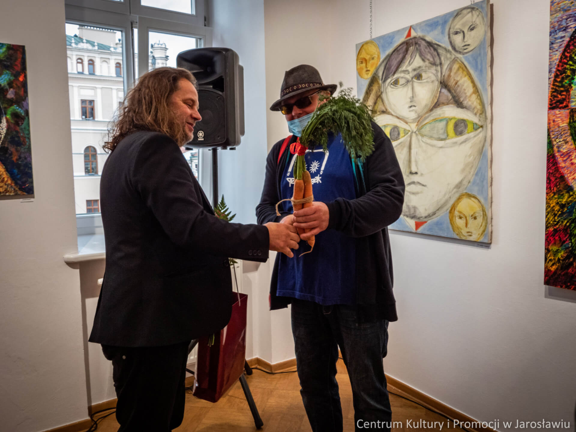 przyjaciel artysty wrecza mu wiązanke marchewek podczas wernisazu