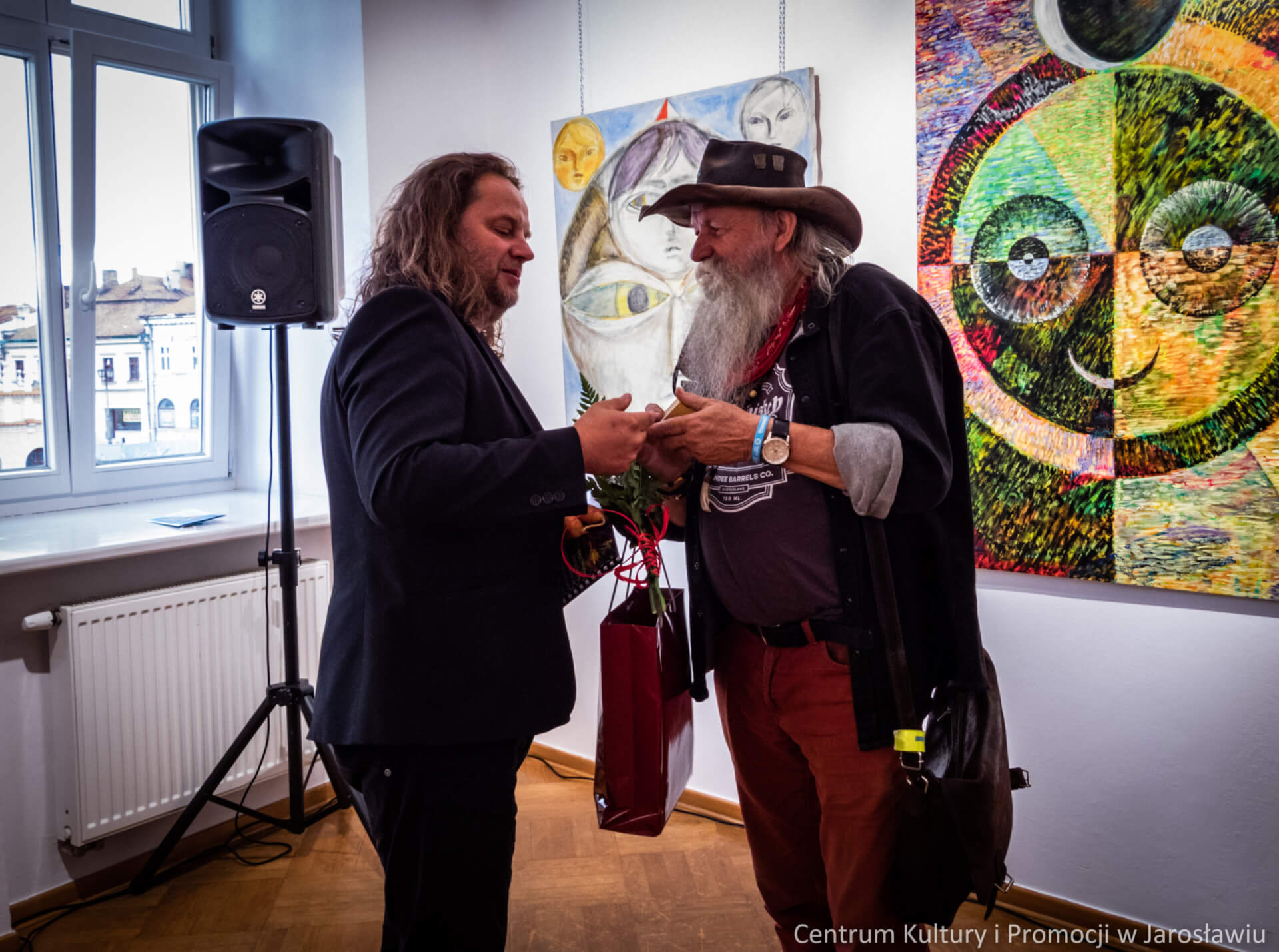 przyjaciel artysty wręcza mu prezent podczas wernisażu