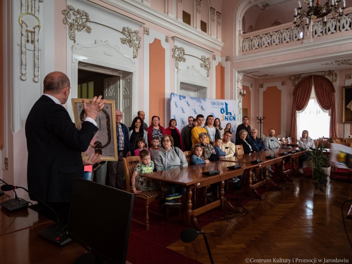 zwiedzanie Sali Narad, w tle zastępca burmistrza miasta, radny rady miasta oraz przewodnik po ratuszu