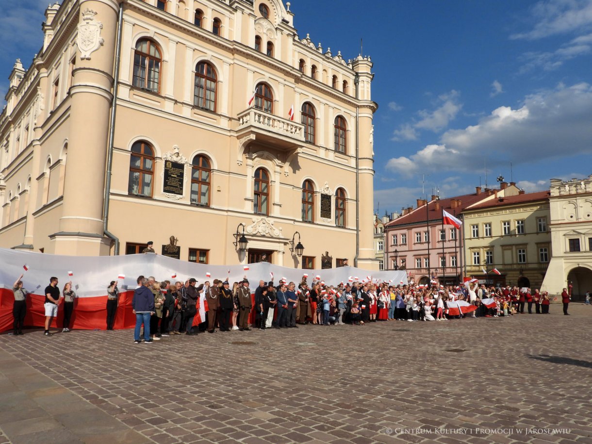 Początek maja to czas upamiętniający jedne z najważniejszych wydarzeń i symboli w naszej historii. Od 2004 roku w całej Polsce, 2 maja obchodzimy Dzień Flagi RP natomiast 3 maja przypada Święto Narodowe Trzeciego Maja. Dzień Flag RP to święto wprowadzone na mocy ustawy z 20 lutego 2004 r. Jarosławskie obchody Święta Flagi RP rozpoczęły się uroczystym przemarszem z placu ks. Piotra Skargi na jarosławski Rynek. Biało-czerwony korowód niosący 30-metrową flagę prowadzony był przez Orkiestrę Dętą „Laudate Dominum” oraz kompanię reprezentacyjna Wojska Polskiego. Po dotarciu na rynek, uroczyście podniesiono flagę na masz. Towarzyszył temu odegrany przez „Laudate Dominum” oraz odśpiewany przez żołnierzy i wszystkich zebranych Mazurek Dąbrowskiego. Okolicznościowe przemówienie wygłosił min. Burmistrz Miasta Jarosławia Waldemar Paluch, który podkreślał wagę symboli narodowych w tym szczególnym czasie, po czym miała miejsce defilada wojskowa. Na zakończenie obchodów rozdane zostały biało-czerwone flagi, wykonano wspólne pamiątkowe zdjęcie, a dzieci mogły wziąć udział w specjalnie dla nich przygotowanych animacjach i zabawach. Święto Narodowe Trzeciego Maja otworzył koncert Reprezentacyjnego Chóru Mieszanego „Jarosław”, który poprzedził mszę święto w intencji Ojczyzny, odprawioną w kościele p.w. NMP Królowej Polski. Po eucharystii udano się pod pomnik Konstytucji Trzeciego Maja gdzie w towarzystwie Mazurka Dąbrowskiego podniesiono flagę na maszt. Po okolicznościowych przemówieniach odczytana apel pamięci, następnie kompania honorowa Wojska Polskiego oddała salwę honorową. Później nastąpiło złożenie kwiatów pod Pomnikiem przez władze parlamentarzystów, władze wojewódzkie i samorządowe, służby i instytucje publiczne, organizacje pozarządowe oraz szkoły.