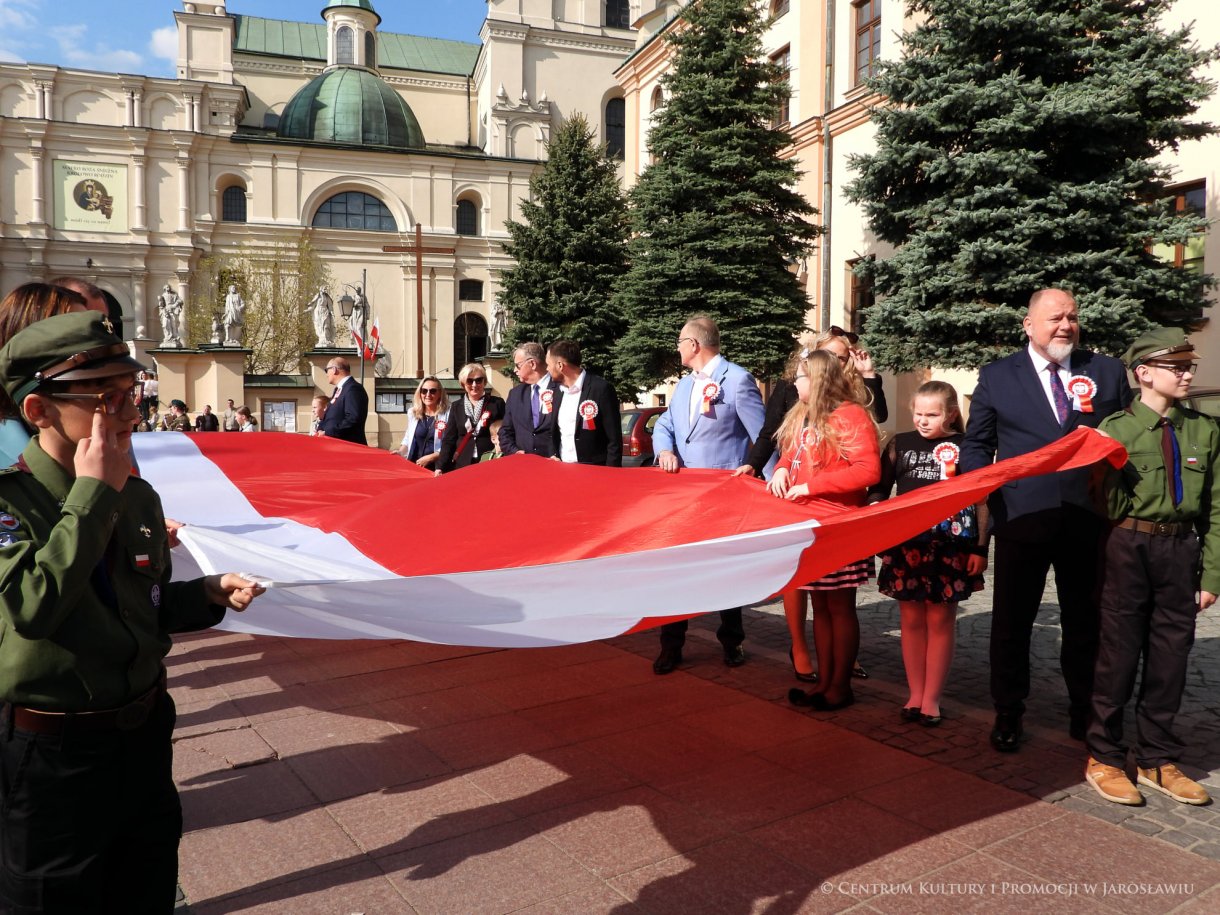 Początek maja to czas upamiętniający jedne z najważniejszych wydarzeń i symboli w naszej historii. Od 2004 roku w całej Polsce, 2 maja obchodzimy Dzień Flagi RP natomiast 3 maja przypada Święto Narodowe Trzeciego Maja. Dzień Flag RP to święto wprowadzone na mocy ustawy z 20 lutego 2004 r. Jarosławskie obchody Święta Flagi RP rozpoczęły się uroczystym przemarszem z placu ks. Piotra Skargi na jarosławski Rynek. Biało-czerwony korowód niosący 30-metrową flagę prowadzony był przez Orkiestrę Dętą „Laudate Dominum” oraz kompanię reprezentacyjna Wojska Polskiego. Po dotarciu na rynek, uroczyście podniesiono flagę na masz. Towarzyszył temu odegrany przez „Laudate Dominum” oraz odśpiewany przez żołnierzy i wszystkich zebranych Mazurek Dąbrowskiego. Okolicznościowe przemówienie wygłosił min. Burmistrz Miasta Jarosławia Waldemar Paluch, który podkreślał wagę symboli narodowych w tym szczególnym czasie, po czym miała miejsce defilada wojskowa. Na zakończenie obchodów rozdane zostały biało-czerwone flagi, wykonano wspólne pamiątkowe zdjęcie, a dzieci mogły wziąć udział w specjalnie dla nich przygotowanych animacjach i zabawach. Święto Narodowe Trzeciego Maja otworzył koncert Reprezentacyjnego Chóru Mieszanego „Jarosław”, który poprzedził mszę święto w intencji Ojczyzny, odprawioną w kościele p.w. NMP Królowej Polski. Po eucharystii udano się pod pomnik Konstytucji Trzeciego Maja gdzie w towarzystwie Mazurka Dąbrowskiego podniesiono flagę na maszt. Po okolicznościowych przemówieniach odczytana apel pamięci, następnie kompania honorowa Wojska Polskiego oddała salwę honorową. Później nastąpiło złożenie kwiatów pod Pomnikiem przez władze parlamentarzystów, władze wojewódzkie i samorządowe, służby i instytucje publiczne, organizacje pozarządowe oraz szkoły.