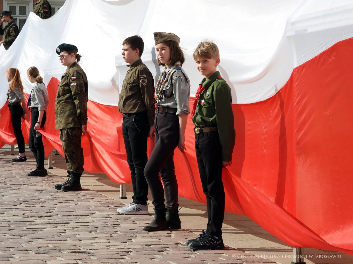 Początek maja to czas upamiętniający jedne z najważniejszych wydarzeń i symboli w naszej historii. Od 2004 roku w całej Polsce, 2 maja obchodzimy Dzień Flagi RP natomiast 3 maja przypada Święto Narodowe Trzeciego Maja. Dzień Flag RP to święto wprowadzone na mocy ustawy z 20 lutego 2004 r. Jarosławskie obchody Święta Flagi RP rozpoczęły się uroczystym przemarszem z placu ks. Piotra Skargi na jarosławski Rynek. Biało-czerwony korowód niosący 30-metrową flagę prowadzony był przez Orkiestrę Dętą „Laudate Dominum” oraz kompanię reprezentacyjna Wojska Polskiego. Po dotarciu na rynek, uroczyście podniesiono flagę na masz. Towarzyszył temu odegrany przez „Laudate Dominum” oraz odśpiewany przez żołnierzy i wszystkich zebranych Mazurek Dąbrowskiego. Okolicznościowe przemówienie wygłosił min. Burmistrz Miasta Jarosławia Waldemar Paluch, który podkreślał wagę symboli narodowych w tym szczególnym czasie, po czym miała miejsce defilada wojskowa. Na zakończenie obchodów rozdane zostały biało-czerwone flagi, wykonano wspólne pamiątkowe zdjęcie, a dzieci mogły wziąć udział w specjalnie dla nich przygotowanych animacjach i zabawach. Święto Narodowe Trzeciego Maja otworzył koncert Reprezentacyjnego Chóru Mieszanego „Jarosław”, który poprzedził mszę święto w intencji Ojczyzny, odprawioną w kościele p.w. NMP Królowej Polski. Po eucharystii udano się pod pomnik Konstytucji Trzeciego Maja gdzie w towarzystwie Mazurka Dąbrowskiego podniesiono flagę na maszt. Po okolicznościowych przemówieniach odczytana apel pamięci, następnie kompania honorowa Wojska Polskiego oddała salwę honorową. Później nastąpiło złożenie kwiatów pod Pomnikiem przez władze parlamentarzystów, władze wojewódzkie i samorządowe, służby i instytucje publiczne, organizacje pozarządowe oraz szkoły.