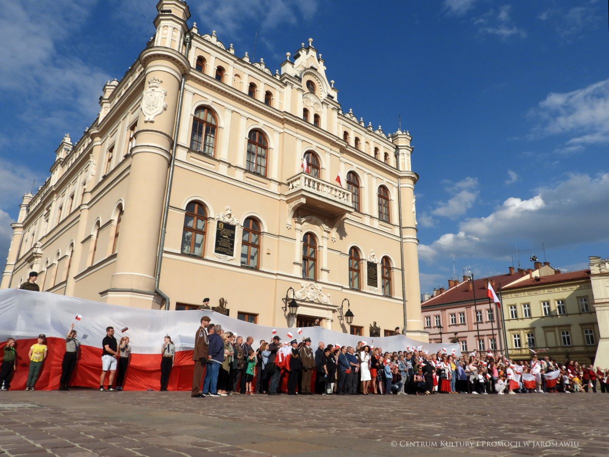 Początek maja to czas upamiętniający jedne z najważniejszych wydarzeń i symboli w naszej historii. Od 2004 roku w całej Polsce, 2 maja obchodzimy Dzień Flagi RP natomiast 3 maja przypada Święto Narodowe Trzeciego Maja. Dzień Flag RP to święto wprowadzone na mocy ustawy z 20 lutego 2004 r. Jarosławskie obchody Święta Flagi RP rozpoczęły się uroczystym przemarszem z placu ks. Piotra Skargi na jarosławski Rynek. Biało-czerwony korowód niosący 30-metrową flagę prowadzony był przez Orkiestrę Dętą „Laudate Dominum” oraz kompanię reprezentacyjna Wojska Polskiego. Po dotarciu na rynek, uroczyście podniesiono flagę na masz. Towarzyszył temu odegrany przez „Laudate Dominum” oraz odśpiewany przez żołnierzy i wszystkich zebranych Mazurek Dąbrowskiego. Okolicznościowe przemówienie wygłosił min. Burmistrz Miasta Jarosławia Waldemar Paluch, który podkreślał wagę symboli narodowych w tym szczególnym czasie, po czym miała miejsce defilada wojskowa. Na zakończenie obchodów rozdane zostały biało-czerwone flagi, wykonano wspólne pamiątkowe zdjęcie, a dzieci mogły wziąć udział w specjalnie dla nich przygotowanych animacjach i zabawach. Święto Narodowe Trzeciego Maja otworzył koncert Reprezentacyjnego Chóru Mieszanego „Jarosław”, który poprzedził mszę święto w intencji Ojczyzny, odprawioną w kościele p.w. NMP Królowej Polski. Po eucharystii udano się pod pomnik Konstytucji Trzeciego Maja gdzie w towarzystwie Mazurka Dąbrowskiego podniesiono flagę na maszt. Po okolicznościowych przemówieniach odczytana apel pamięci, następnie kompania honorowa Wojska Polskiego oddała salwę honorową. Później nastąpiło złożenie kwiatów pod Pomnikiem przez władze parlamentarzystów, władze wojewódzkie i samorządowe, służby i instytucje publiczne, organizacje pozarządowe oraz szkoły.