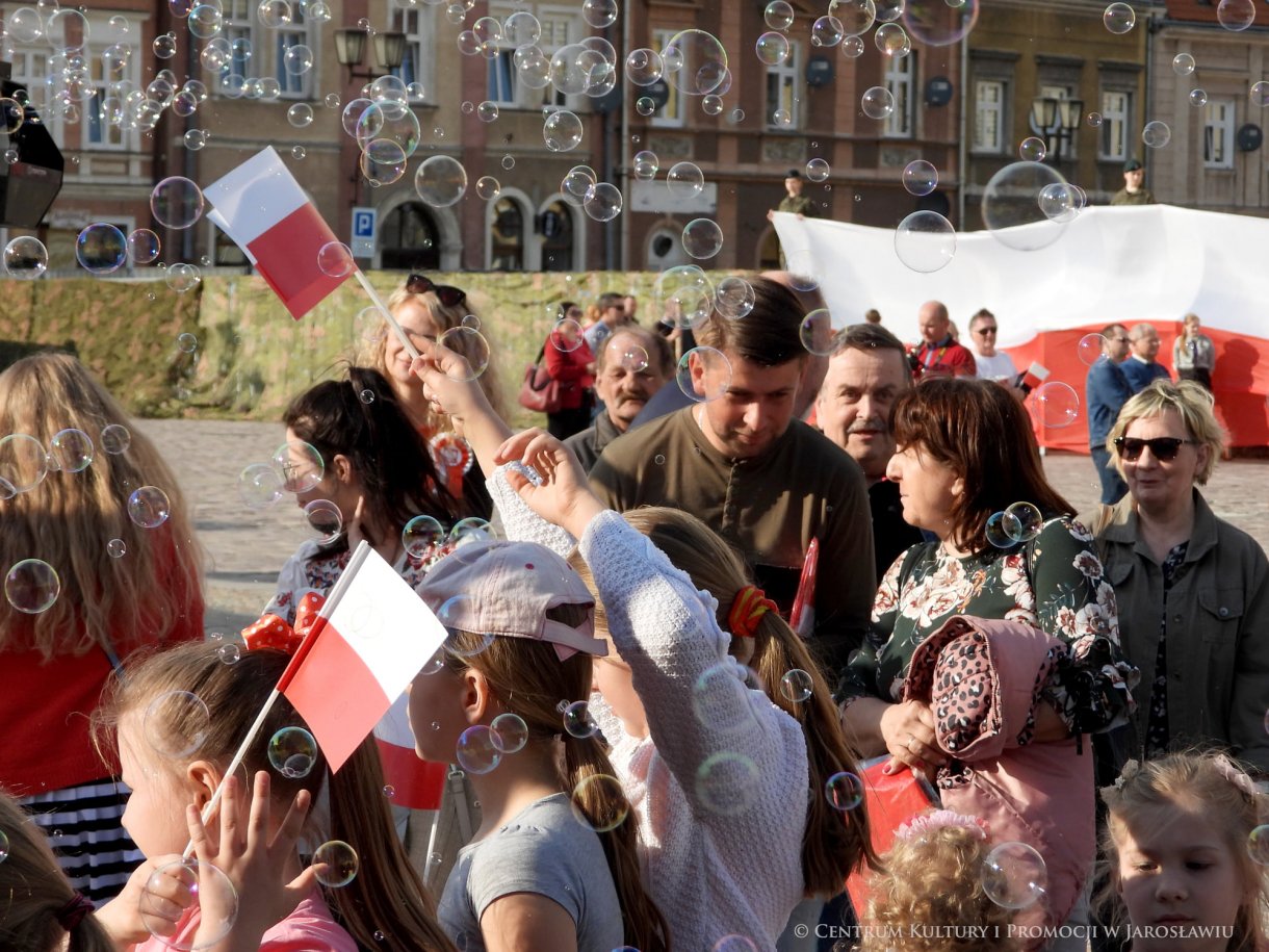 Początek maja to czas upamiętniający jedne z najważniejszych wydarzeń i symboli w naszej historii. Od 2004 roku w całej Polsce, 2 maja obchodzimy Dzień Flagi RP natomiast 3 maja przypada Święto Narodowe Trzeciego Maja. Dzień Flag RP to święto wprowadzone na mocy ustawy z 20 lutego 2004 r. Jarosławskie obchody Święta Flagi RP rozpoczęły się uroczystym przemarszem z placu ks. Piotra Skargi na jarosławski Rynek. Biało-czerwony korowód niosący 30-metrową flagę prowadzony był przez Orkiestrę Dętą „Laudate Dominum” oraz kompanię reprezentacyjna Wojska Polskiego. Po dotarciu na rynek, uroczyście podniesiono flagę na masz. Towarzyszył temu odegrany przez „Laudate Dominum” oraz odśpiewany przez żołnierzy i wszystkich zebranych Mazurek Dąbrowskiego. Okolicznościowe przemówienie wygłosił min. Burmistrz Miasta Jarosławia Waldemar Paluch, który podkreślał wagę symboli narodowych w tym szczególnym czasie, po czym miała miejsce defilada wojskowa. Na zakończenie obchodów rozdane zostały biało-czerwone flagi, wykonano wspólne pamiątkowe zdjęcie, a dzieci mogły wziąć udział w specjalnie dla nich przygotowanych animacjach i zabawach. Święto Narodowe Trzeciego Maja otworzył koncert Reprezentacyjnego Chóru Mieszanego „Jarosław”, który poprzedził mszę święto w intencji Ojczyzny, odprawioną w kościele p.w. NMP Królowej Polski. Po eucharystii udano się pod pomnik Konstytucji Trzeciego Maja gdzie w towarzystwie Mazurka Dąbrowskiego podniesiono flagę na maszt. Po okolicznościowych przemówieniach odczytana apel pamięci, następnie kompania honorowa Wojska Polskiego oddała salwę honorową. Później nastąpiło złożenie kwiatów pod Pomnikiem przez władze parlamentarzystów, władze wojewódzkie i samorządowe, służby i instytucje publiczne, organizacje pozarządowe oraz szkoły.