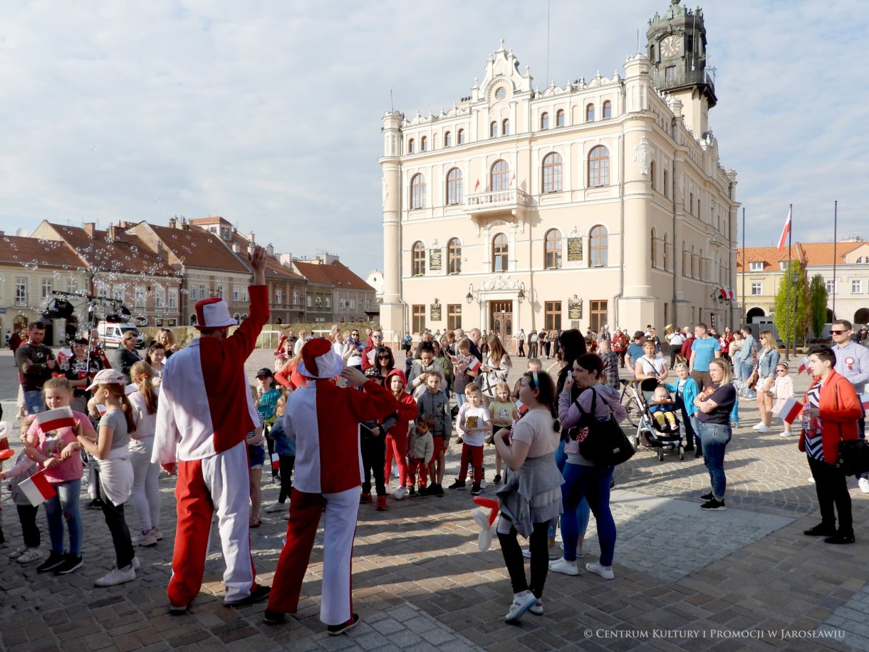 Początek maja to czas upamiętniający jedne z najważniejszych wydarzeń i symboli w naszej historii. Od 2004 roku w całej Polsce, 2 maja obchodzimy Dzień Flagi RP natomiast 3 maja przypada Święto Narodowe Trzeciego Maja. Dzień Flag RP to święto wprowadzone na mocy ustawy z 20 lutego 2004 r. Jarosławskie obchody Święta Flagi RP rozpoczęły się uroczystym przemarszem z placu ks. Piotra Skargi na jarosławski Rynek. Biało-czerwony korowód niosący 30-metrową flagę prowadzony był przez Orkiestrę Dętą „Laudate Dominum” oraz kompanię reprezentacyjna Wojska Polskiego. Po dotarciu na rynek, uroczyście podniesiono flagę na masz. Towarzyszył temu odegrany przez „Laudate Dominum” oraz odśpiewany przez żołnierzy i wszystkich zebranych Mazurek Dąbrowskiego. Okolicznościowe przemówienie wygłosił min. Burmistrz Miasta Jarosławia Waldemar Paluch, który podkreślał wagę symboli narodowych w tym szczególnym czasie, po czym miała miejsce defilada wojskowa. Na zakończenie obchodów rozdane zostały biało-czerwone flagi, wykonano wspólne pamiątkowe zdjęcie, a dzieci mogły wziąć udział w specjalnie dla nich przygotowanych animacjach i zabawach. Święto Narodowe Trzeciego Maja otworzył koncert Reprezentacyjnego Chóru Mieszanego „Jarosław”, który poprzedził mszę święto w intencji Ojczyzny, odprawioną w kościele p.w. NMP Królowej Polski. Po eucharystii udano się pod pomnik Konstytucji Trzeciego Maja gdzie w towarzystwie Mazurka Dąbrowskiego podniesiono flagę na maszt. Po okolicznościowych przemówieniach odczytana apel pamięci, następnie kompania honorowa Wojska Polskiego oddała salwę honorową. Później nastąpiło złożenie kwiatów pod Pomnikiem przez władze parlamentarzystów, władze wojewódzkie i samorządowe, służby i instytucje publiczne, organizacje pozarządowe oraz szkoły.