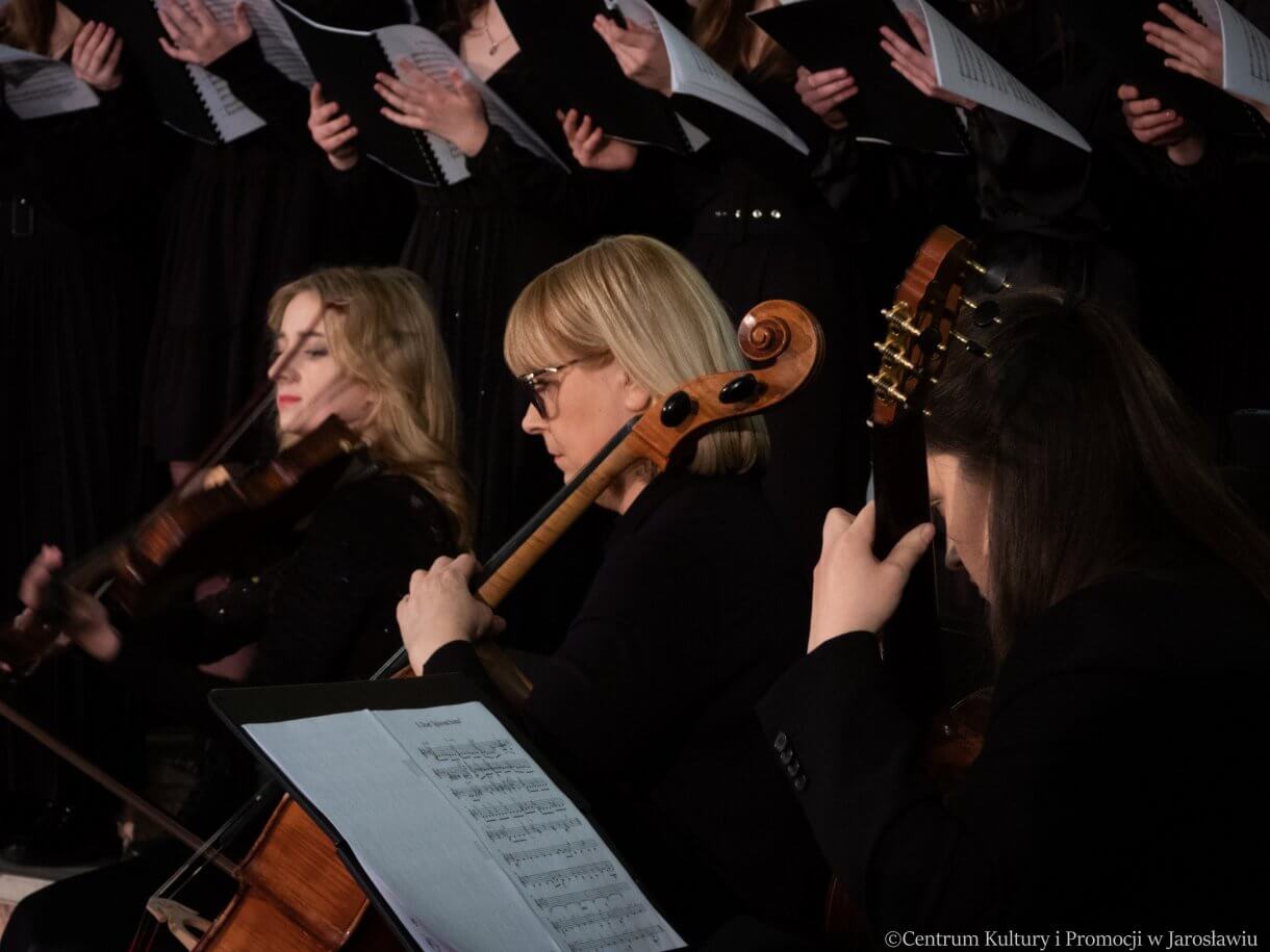 Koncert w kolegiacie -Skrzypaczka, wiolonczelistka, gitarzystka, w tle ręce chóru