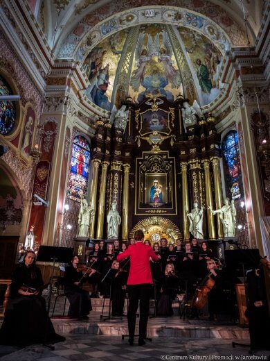 Stabat Mater dolorosa Koncert w kolegiacie - wykonawcy, w czerwonym ubrani dyrygentka, w tle ołtarz w kolegiacie