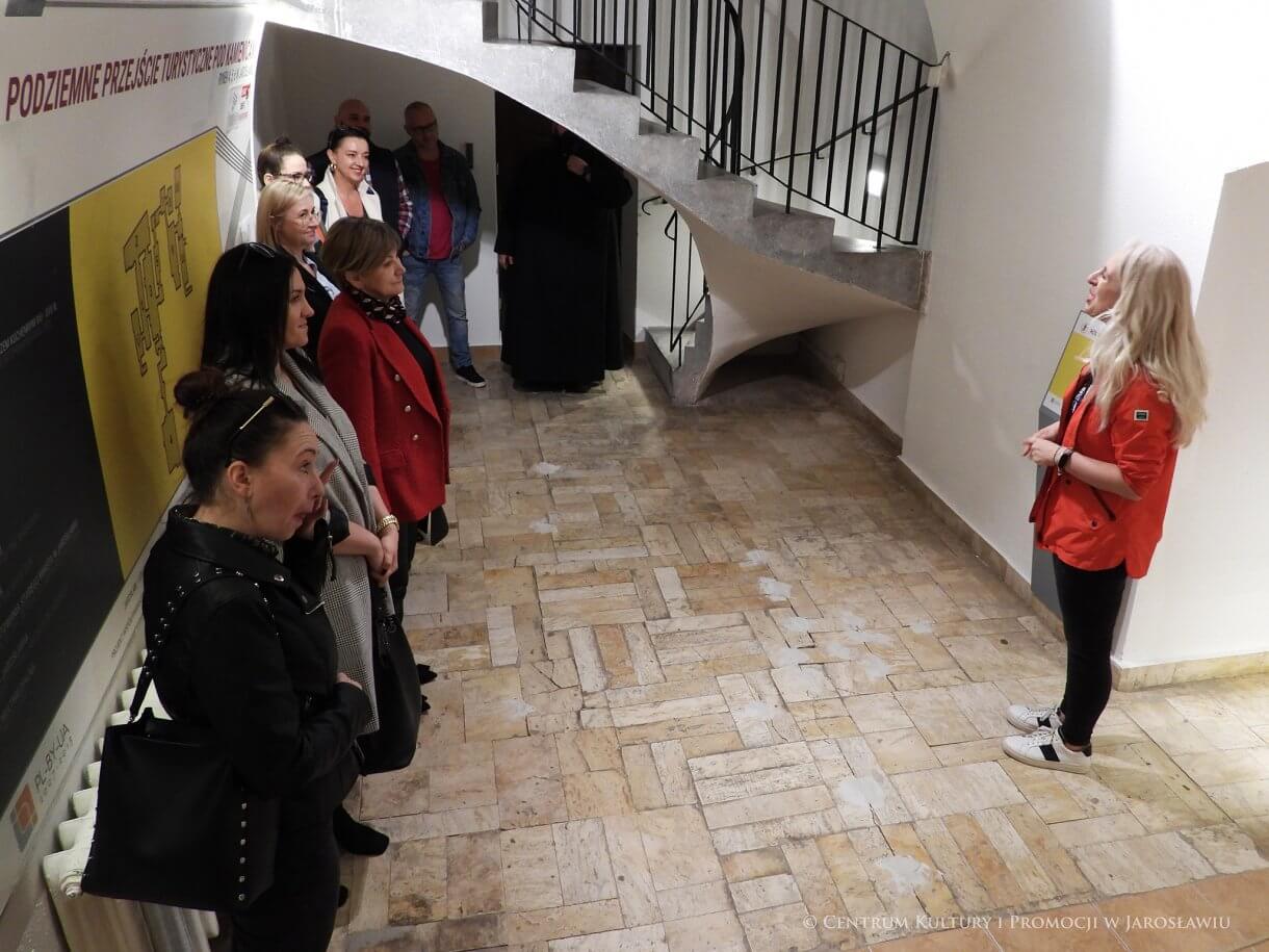 Grupa ludzi w Podziemnym Przejściu Turystycznym, z prawej przewodniczka z czerwonej kurtce