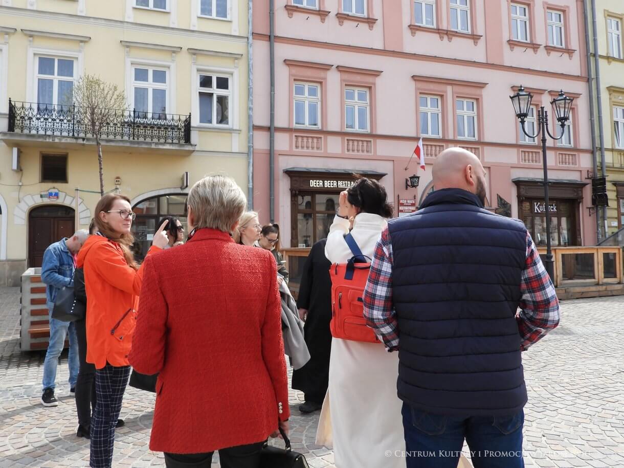 Grupa ludzi na płycie rynku, w tle kamienice