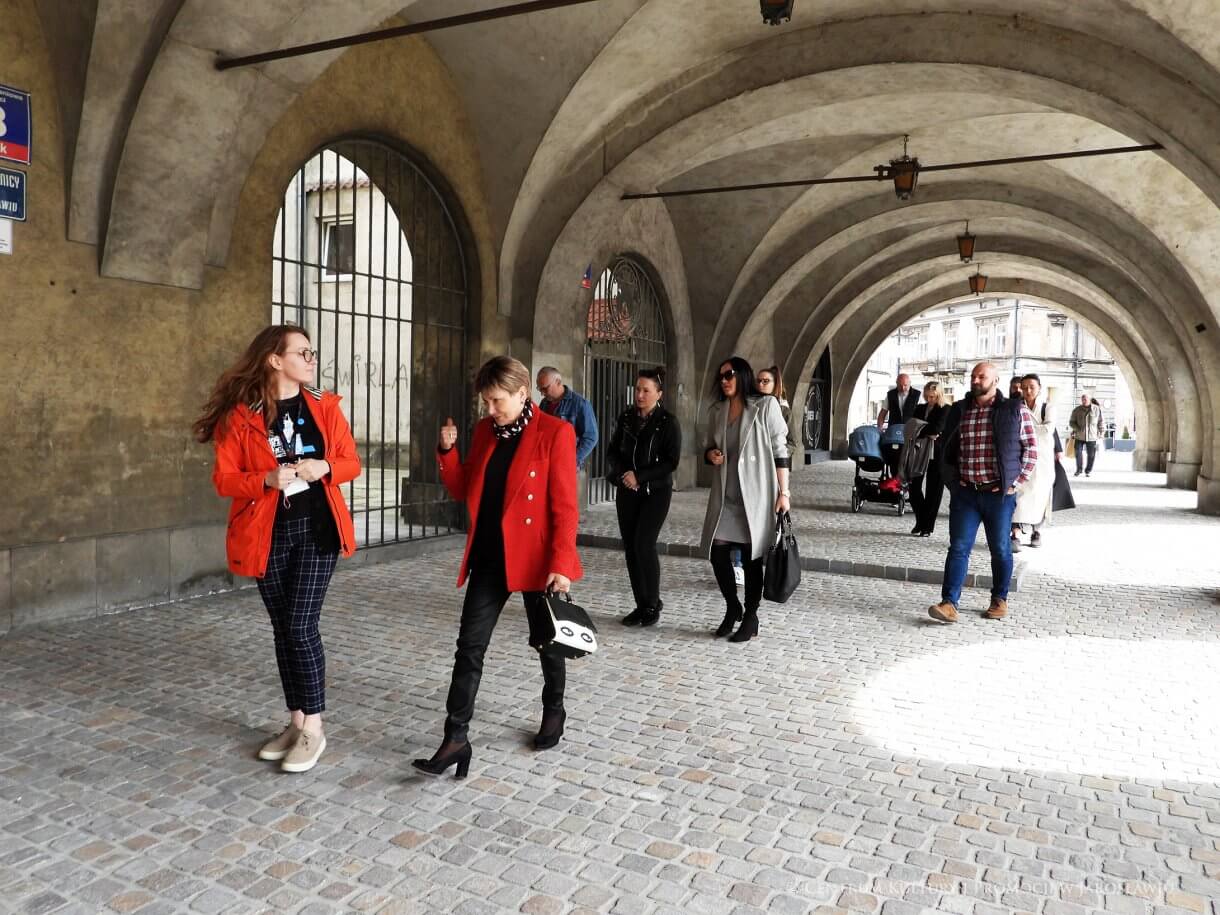Grupa ludzi w podcieniach kamienicy, z lewej przewodniczka